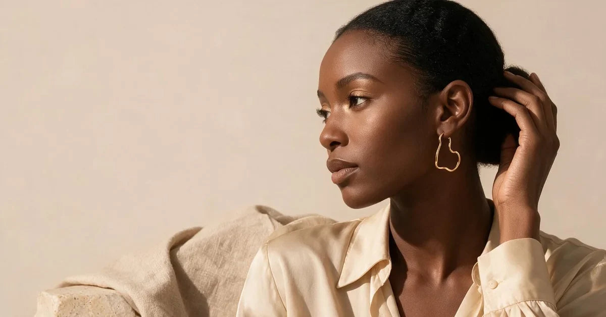 Hoop earrings on a model: gold-tone irregular wave hoop earrings with a cream silk blouse