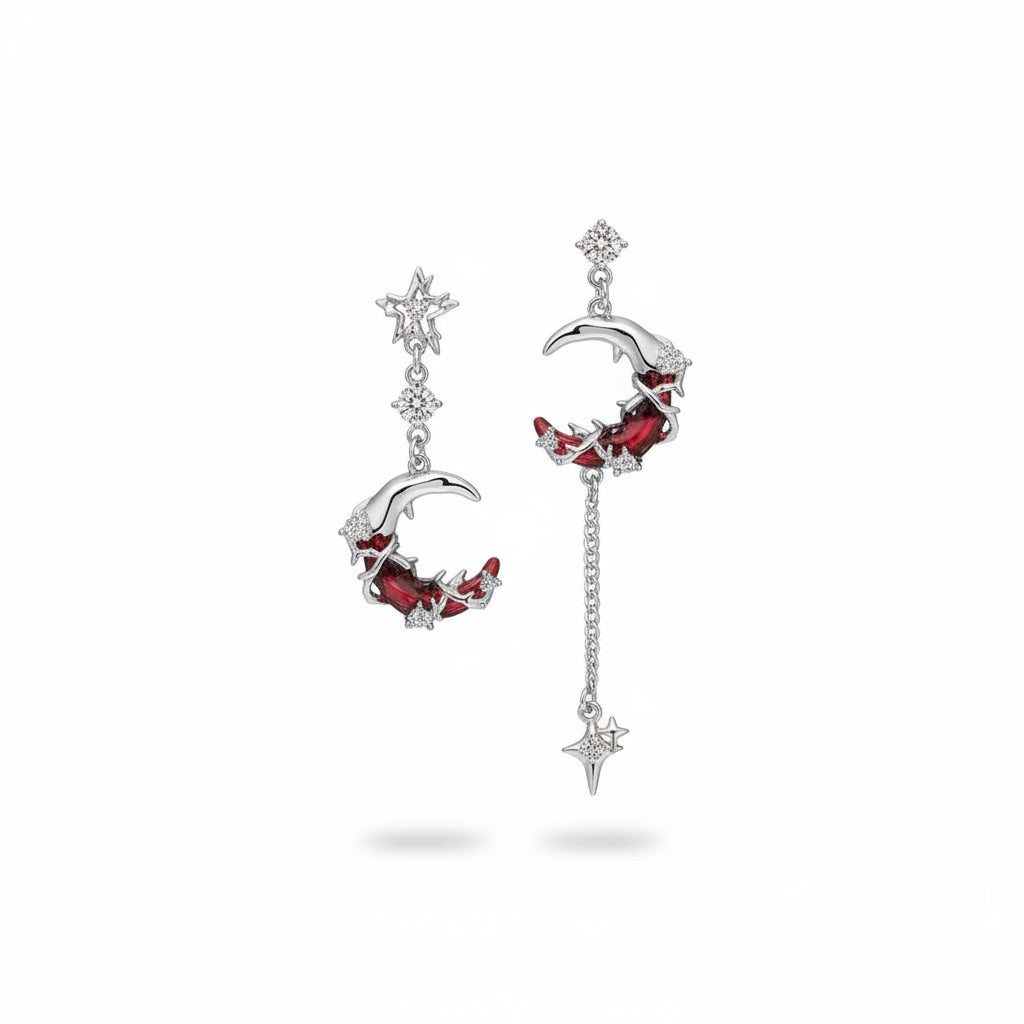 Asymmetric silver-tone copper zircon moon and star drop earrings: left earring with hollow eight-pointed star stud, round zircon connector and crescent moon pendant set with deep red and white zircon in thorn texture; right earring with round zircon stud, matching crescent moon pendant, silver chain drop and four-pointed spike star charm; isolated on white background with soft drop shadow

