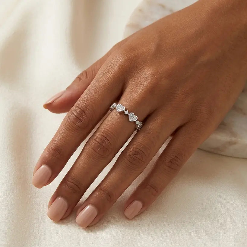 Woman wearing silver alloy adjustable open band heart zirconia ring on middle finger, hand resting naturally on cream satin fabric in soft natural light