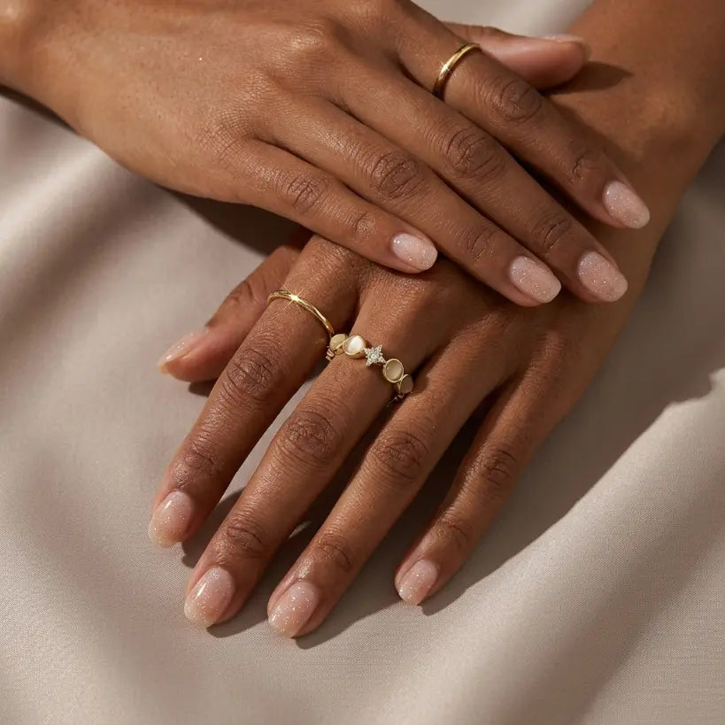 Woman with medium skin tone wearing 18K gold plated cat eye stone and star zirconia open band ring on index finger, hands crossed and resting on cream satin fabric, with a plain gold band ring on the other hand

