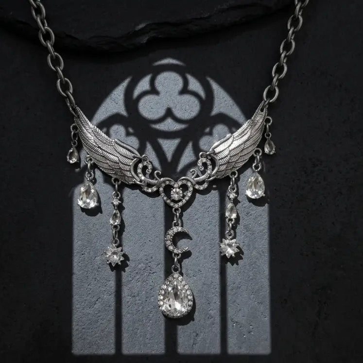 Gothic silver-tone angel wing heart moon rhinestone drop necklace with detailed feather wings, rhinestone heart, crescent moon and large pear crystal halo drop, displayed on dark grey stone surface with dramatic gothic trefoil arch window shadow projection, strong directional spotlight, black background, AI-generated image

