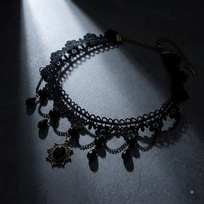 Gothic black lace choker necklace with draped antique bronze chains, black faceted teardrop crystal bead drops and sunburst filigree black gemstone pendant with small key charm, displayed on dark blue-grey stone surface with dramatic single spotlight beam, black background, AI-generated image


