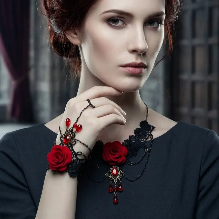 Woman with light skin tone and dark auburn updo wearing gothic black lace red rose crystal slave bracelet ring set on wrist and finger, paired with matching gothic black lace red rose crystal choker necklace at neck, dark grey round-neck top, dark gothic window background, AI-generated model image — bracelet ring set shown as part of coordinated gothic jewelry set

