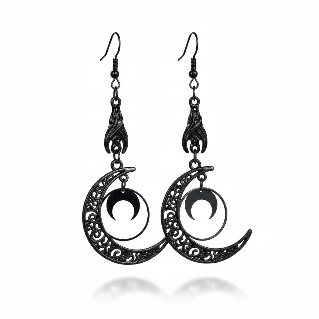 Pair of gothic gunmetal black alloy crescent moon drop earrings with black fish hook ear wire, black filigree flame claw connector with scrollwork, large hollow crescent moon pendant with swirl filigree cutout, and small solid crescent moon charm suspended inside circular frame; double-layer nested moon design; isolated on white background with soft drop shadow

