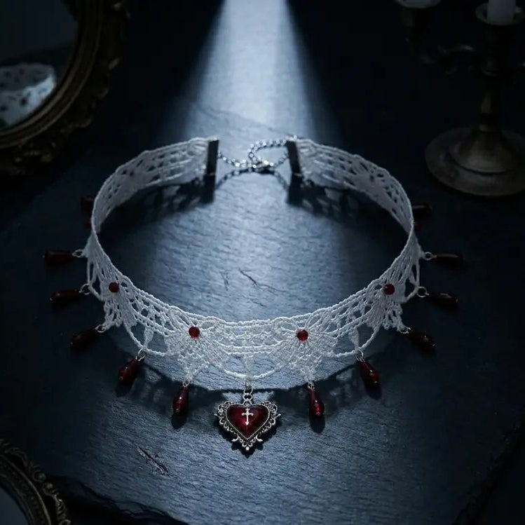 Gothic white lace choker necklace with red teardrop bead drops and silver filigree heart cross pendant, displayed on dark blue-grey stone slab with antique bronze mirror frame and candelabra props, dramatic single spotlight, black background, AI-generated image