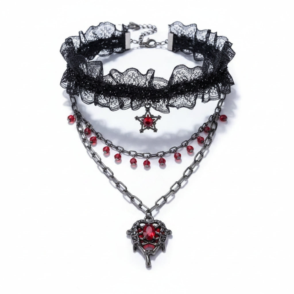Gothic 3-layer necklace set on white background: black lace ruffle choker with red crystal bead drops and pentagram red crystal charm; gunmetal oval link chain with red crystal teardrop fringe; gunmetal oval link chain with gothic filigree winged heart pendant set with large oval red crystal; lobster clasp and extender chain visible, soft drop shadow