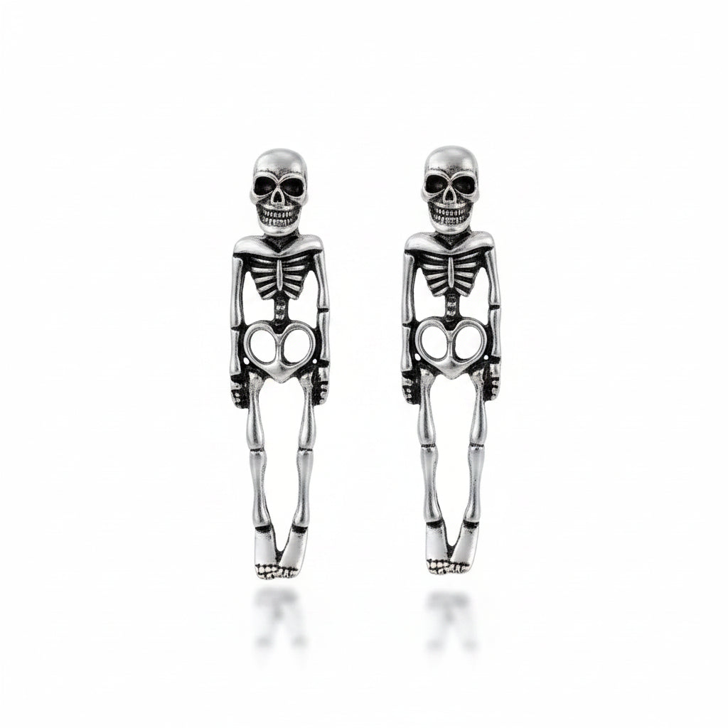 Pair of gothic antique silver-tone alloy full-body skeleton figure stud earrings with detailed skull head stud top, engraved ribcage and spine, hollow heart-shaped pelvis and articulated leg bones; isolated on white background with soft drop shadow

