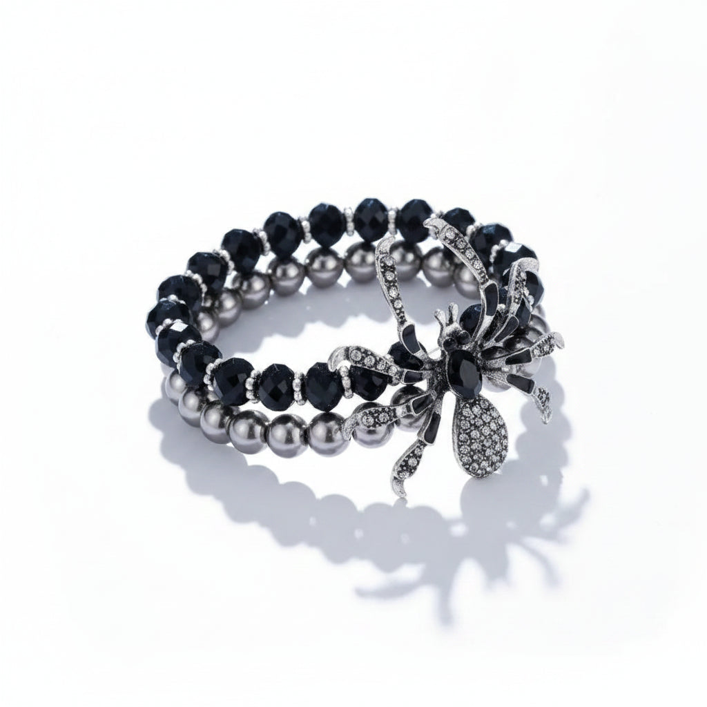 Gothic double-layer stretch bracelet set with black faceted crystal beads and grey faux pearl beads, featuring gunmetal rhinestone spider charm with black oval gemstone body and crystal-set legs, isolated on white background with directional shadow

