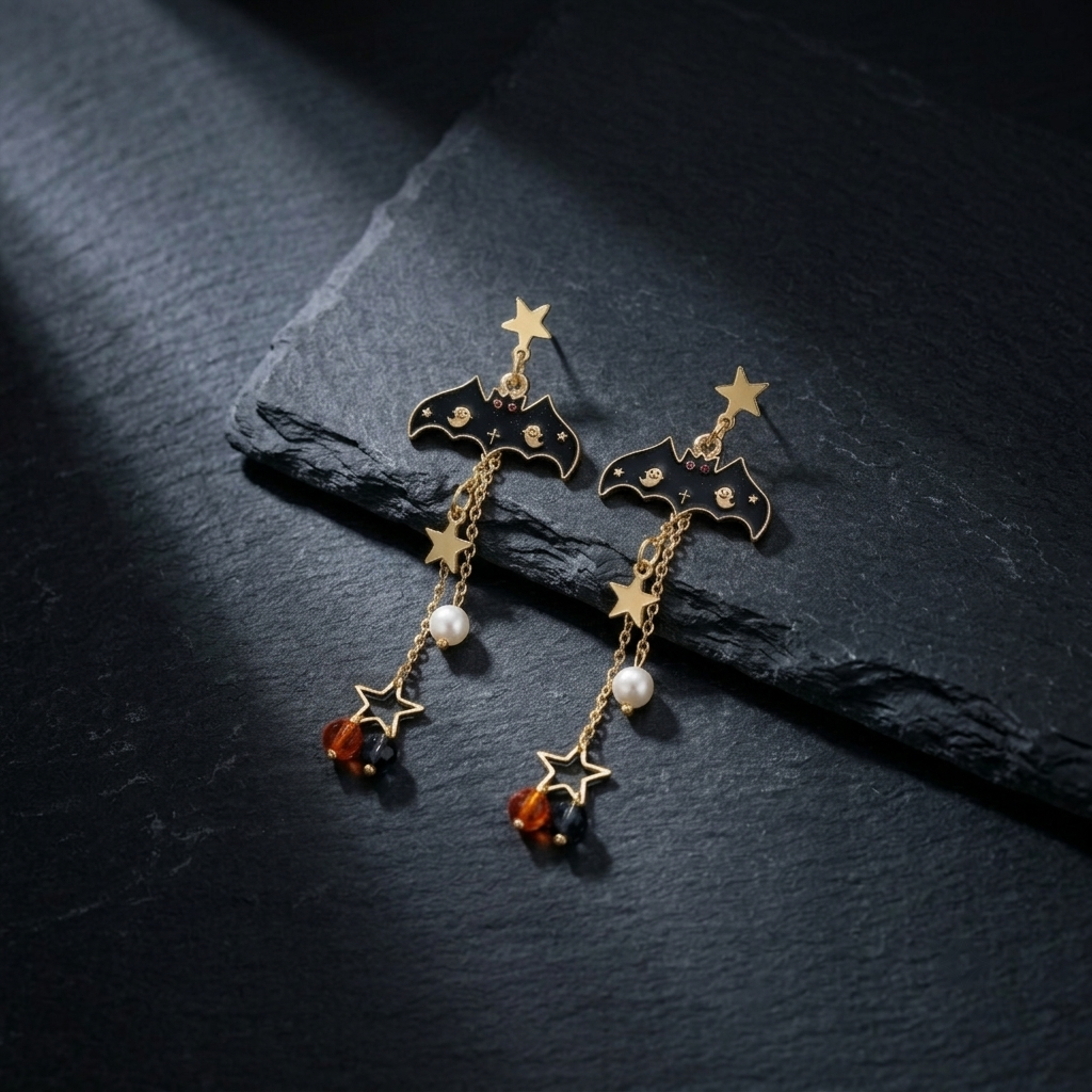 Pair of Halloween gold-tone bat star beaded drop stud earrings leaning against black rough layered rock slab — gold star stud, black enamel bat pendant with ghost skull relief, dual gold chains with pearl, open star frame and amber black crystal bead drops — dramatic single spotlight from upper left, dark black stone background

