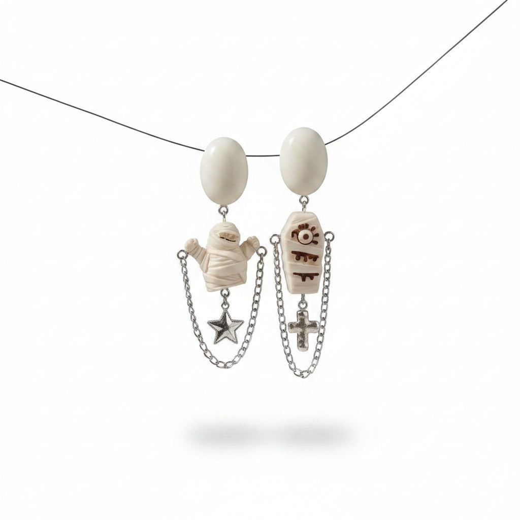 Halloween asymmetric resin drop stud earring set: left earring with white oval resin stud, white resin mummy figure pendant with raised arms and silver double chain star drop; right earring with white oval resin stud, white resin coffin pendant with eye cross and drip relief carving and silver double chain cross drop; isolated on white background, AI-generated product image

