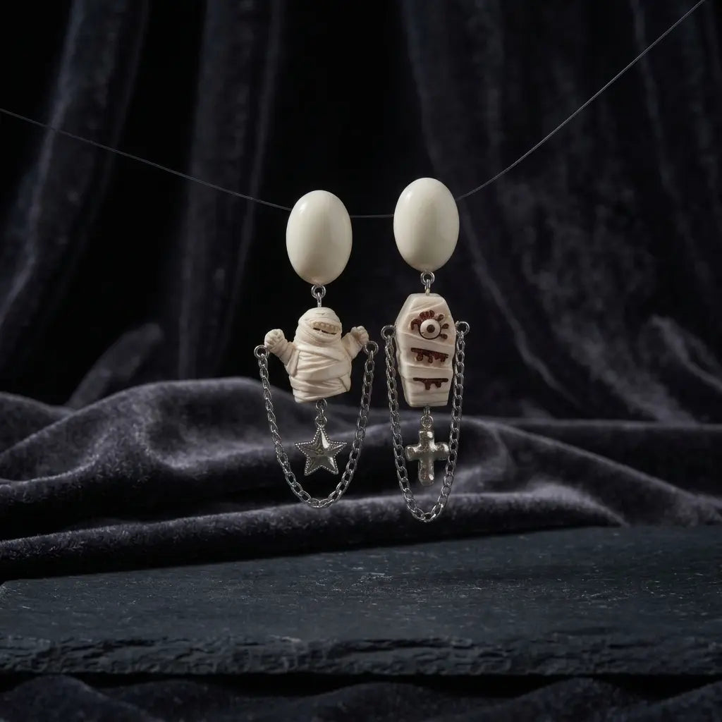 Halloween asymmetric resin drop stud earring set suspended on wire — white resin mummy figure with silver double chain and star drop (left) and white resin coffin with eye cross drip relief and silver double chain cross drop (right) — displayed against dark grey velvet fabric backdrop on dark stone surface with soft ambient light, AI-generated image

