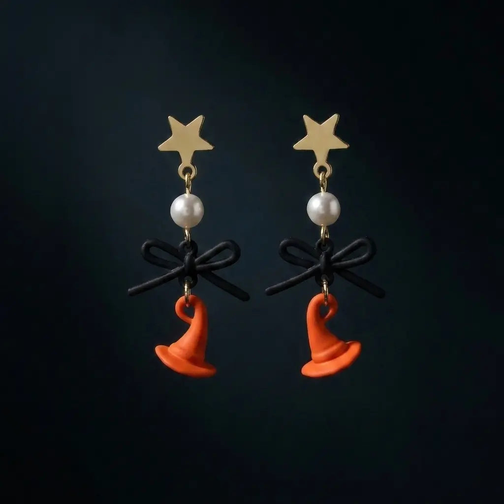 Pair of Halloween gold-tone star stud drop earrings with white faux pearl bead, matte black bow and orange enamel witch hat pendant, displayed flat on dark blue-black gradient background with soft center lighting

