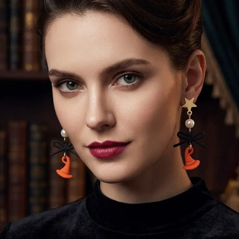 Woman with light skin tone and dark brown updo wearing Halloween gold-tone star stud drop earrings with white faux pearl bead, matte black bow and orange enamel witch hat pendant on both ears, deep burgundy lips, smoky eye makeup, black turtleneck top, dark gothic library with green drape background, AI-generated model image

