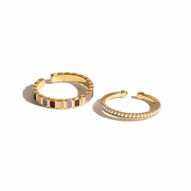 Two gold alloy adjustable open band rings displayed side by side: left with alternating lavender, brown, and cream rectangular enamel tiles; right with continuous row of freshwater pearls in gold beaded frame, isolated on white background

