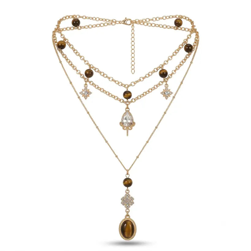 Gold double layer necklace set on white background: upper double chain with tiger eye stone beads, rhinestone star charms and pear-cut zirconia drop pendant; lower Y-drop cable chain with tiger eye bead, rhinestone floral connector and oval tiger eye cabochon pendant; lobster clasp and extender chain visible, soft drop shadow

